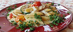 Mediterraner Nudelteller mit knackigem Gemüse, serviert auf der gemütlichen Sonnenterrasse des Landhotels Neuhof.